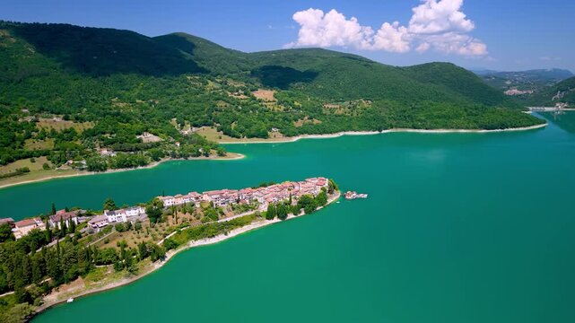 Colle di Tora Turano Lake Italy 4K Drone. Distance fly in approach revealing emerald water lake and long peninsula borgo town from above. Borghi piu belli d Italia most beautiful villages Hidden gems