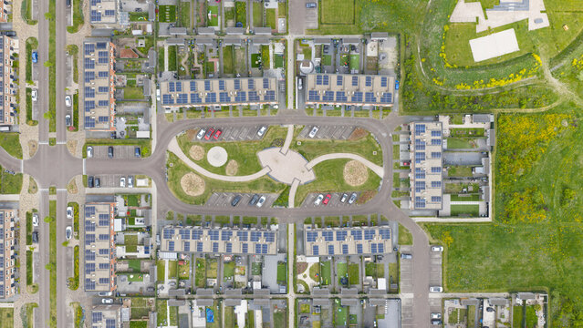 Aerial view of a modern residential neighborhood with terraced houses featuring solar panels on rooftops, green lawns, and a central parking area in Almere, Flevoland, Netherlands.