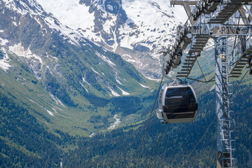 A gondola lift ascends over a vibrant green valley with snow-covered mountains visible in the background under a clear blue sky © Anat art