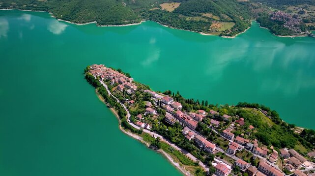 Colle di Tora Turano Lake Rieti Italy 4K Drone. Aerial view over hilltop medieval borgo peninsula village in turquoise water canyon. Borghi piu belli d Italia most beautiful villages travel asset