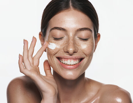 Smiling Young Woman with Freckles Applying Moisturizer to Glowing Skin