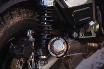 Fototapeta premium Close-up of a dirty motorcycle rear wheel, shock absorber spring and chrome exhaust pipe