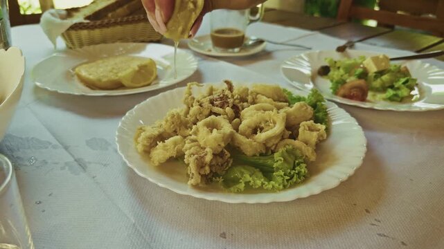 Person Squeezing Fresh Lemon Juice On Fried Calamari Squid Rings. Seafood Appetizer. Mediterranean Cuisine
