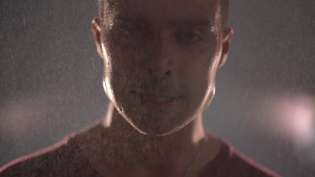 Desperate man holding internal tension under rain at night in dark. Clenching jaw, not screaming, keeping emotions inside. 
