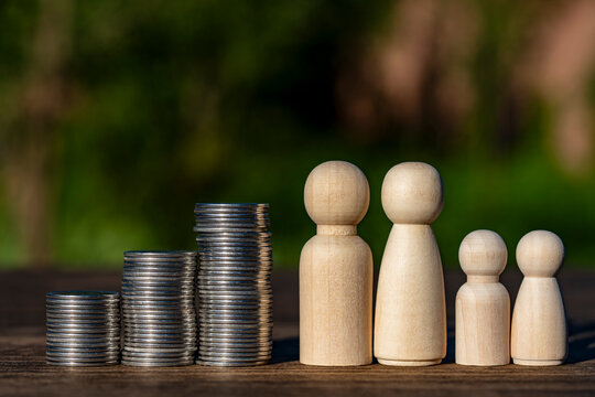 Wooden peg doll family next growing stacks of coins. Small wooden figures family stands beside three rising stacks silver coins with green background representing financial planning and insurance