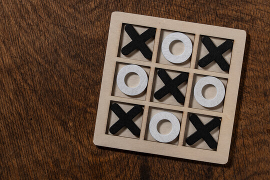 Wooden tic tac toe board game on table. Top view wooden tic tac toe game set filled with black cross and white circle pieces on rustic wooden desk representing strategy logic and business choice