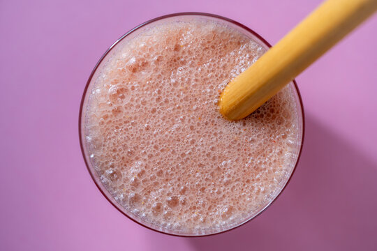 Fresh pink smoothie with bamboo straw. Top view foamy pink fruit smoothie or milkshake in glass with an eco friendly bamboo straw over pastel pink background representing healthy lifestyle