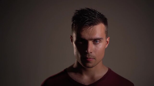 Young man quickly turning head and body to face camera, tense, distrustful expression, ready stance.