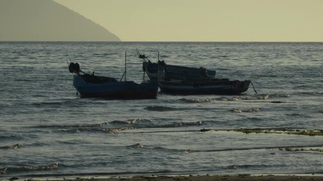 Fishing Boats Anchored In The Sea Near The Shore At Sunset With Mountain In The Background