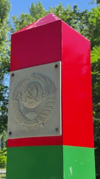 Border Monument with Soviet Emblem: A red and green border monument, featuring a prominent Soviet-era emblem, stands as a historical marker in a natural outdoor setting.