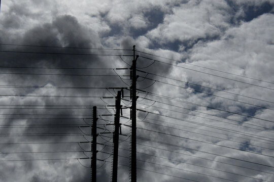 Silhouette of three high voltage transmission pylons against cloudy sky 