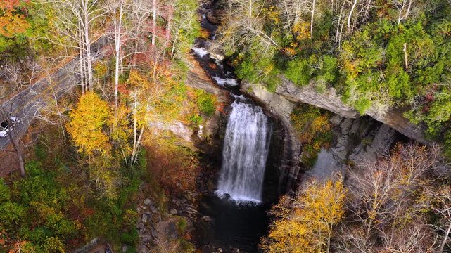 Forest Heritage Scenic Byway and Looking Glass Falls with visitors on the overlook. Cars driving along the scenic roadway through colorful autumn forest.