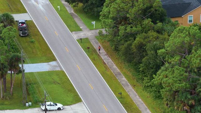 Jogger exercising on residential sidewalk in suburban Florida, captured from above. Dynamic outdoor fitness activity showing movement, determination and healthy living.