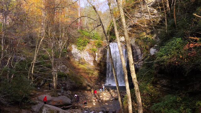 Overhead view of picturesque mountain waterfall flowing through vibrant autumn woodland. People gather at scenic overlook above the cascade and staircase boardwalk.