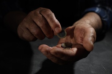 Fototapeta premium Poverty. Homeless senior man counting coins at table in darkness, closeup