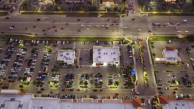 Shopping mall with extensive car parking area and dense vehicle arrangement, illustrating high consumer demand, supply chain flow and economic movement.