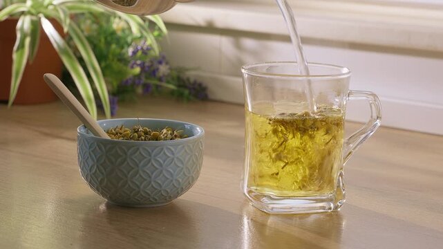 Pouring Dry Chamomile Flowers Into A Glass For Brewing Aromatic And Healthy Herbal Tea