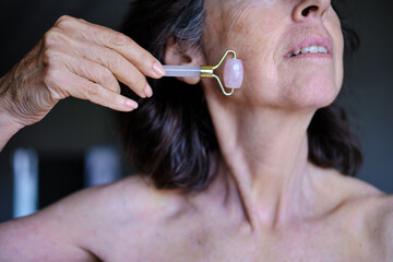 close up shot of Senior woman using rose quartz jade roller on face © Cristina Garcia