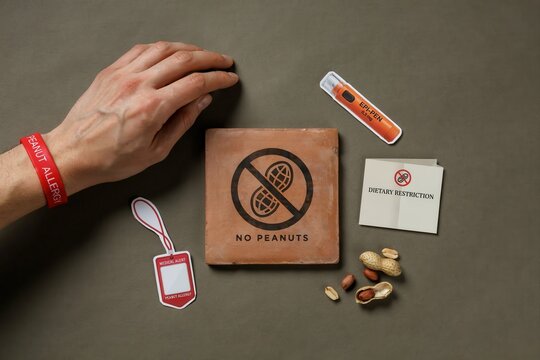 A hand places a coaster with a no peanuts sign next to snacks and labels on a table.