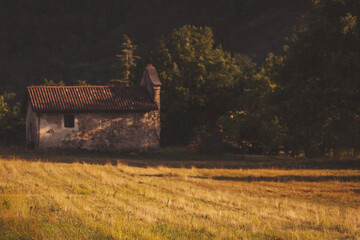 Naklejka premium Charming old stone cottage nestled in a golden field during golden hour, surrounded by lush greenery and serene nature landscapes