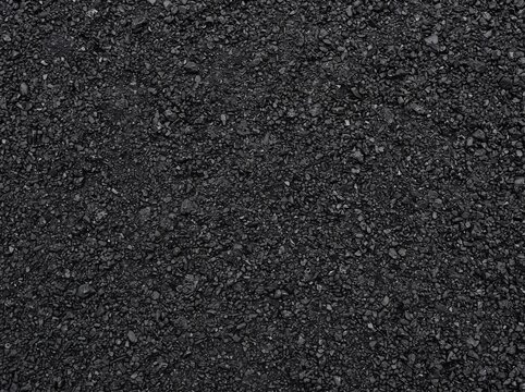 Close-up view of a dark, rough asphalt surface with small stones and granular texture, suitable for roads and paving.