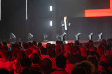 Obraz premium Speaker captivates an audience during dynamic conference presentation with striking red lighting.