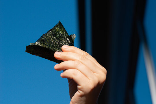onigiri triangle snack dark green nori seaweed held by hand against clear blue sky outdoor setting with copy space for banner design concept of japanese cuisine, healthy eating, street food
