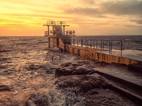 Famous Blackrock diving board, Salthill, Galway city, Ireland. Town popular landmark and watersport spot. Warm orange sunrise color gives the scene vibrant cinematic look and vibe.