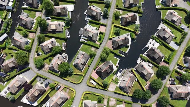 Cinematic 4K drone summer video tilting up from modern thatch-roof holiday villas in Wanneperveen to reveal the wide, green nature reserve of Weerribben-Wieden.