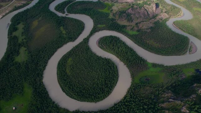 Aerial view of Altai winding river meandering through dense forest and rocky hills.