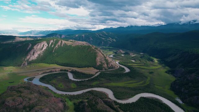Aerial view river meandering through Altai mountain valley and forest with cloudy sky over remote landscape.