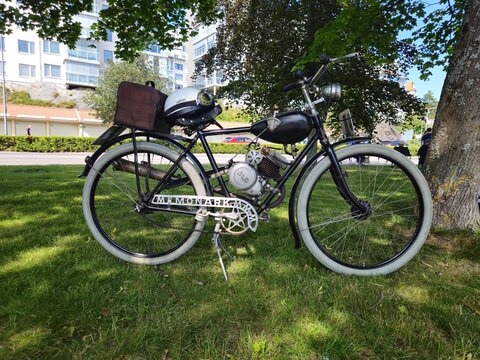 Stockholm County, Sweden, June 27, 2026. Classic car rally. Vintage Motorized Bicycle With Helmet Parked Under Trees.