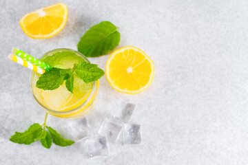 Fototapeta premium Top view of refreshing cold icy beverage, homemade lemonade with fresh lemon slices, mint leaves, ice cubes wtih soda water and condensation in glass on gray background with copy space for text.