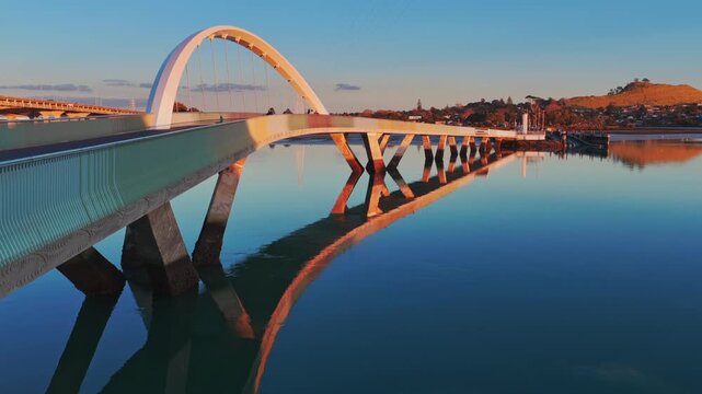 Auckland, New Zealand - The iconic Nga Hau Mangere Bridge, a pedestrian walkway is bathed in the warm glow of sunrise, with a few people enjoying the view.