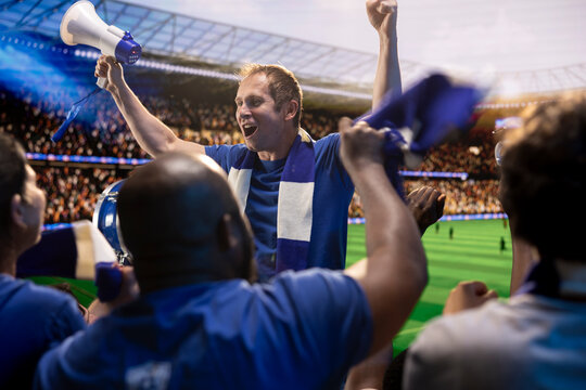 Football supporters raise arms and chant from stadium stands during match day, cheering crowd, scarf.