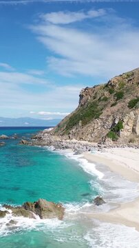Zambrone Beach, Costa degli Dei, Calabria, Italy. Vertical aerial drone footage of turquoise Tyrrhenian Sea, rocky cliffs and white sandy beach on a sunny summer day.