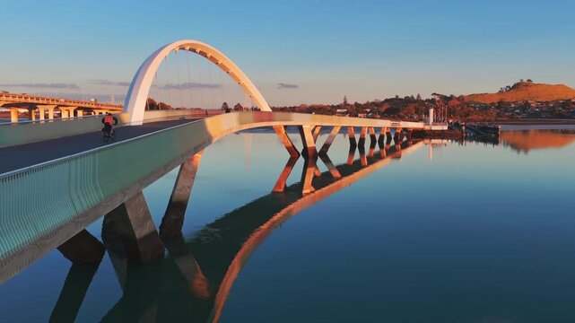 Auckland, New Zealand - The iconic Nga Hau Mangere Bridge is bathed in the warm glow of sunrise as a few early morning anglers cast their lines into the calm waters below.
