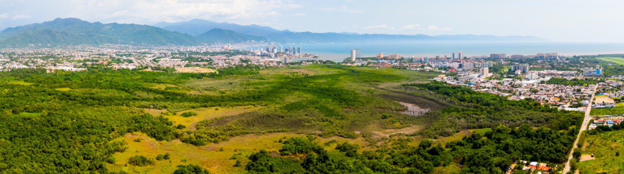 Aerial view of Estero El Salado mangrove protected natural area with lush green vegetation, adjacent to the urban landscape and coastline of Puerto Vallarta, Jalisco, Mexico.