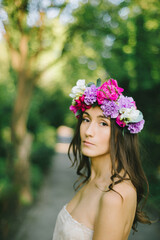 Naklejka premium Close up portrait of a beautiful young girl with flower wreath in a sunny garden