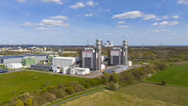 Aerial view of Trianel Gaskraftwerk Hamm power plant with industrial buildings and cooling stacks surrounded by green fields and trees in Hamm, Nordrhein-Westfalen, Germany.