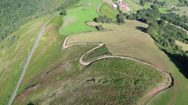 Aerial view of a steep grassy slope with an S-shaped dirt path leading to small village near Saint Jean Pied de Port on the Camino de Santiago, France