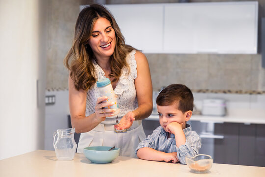 Mother preparing breakfast for reluctant son in kitchen