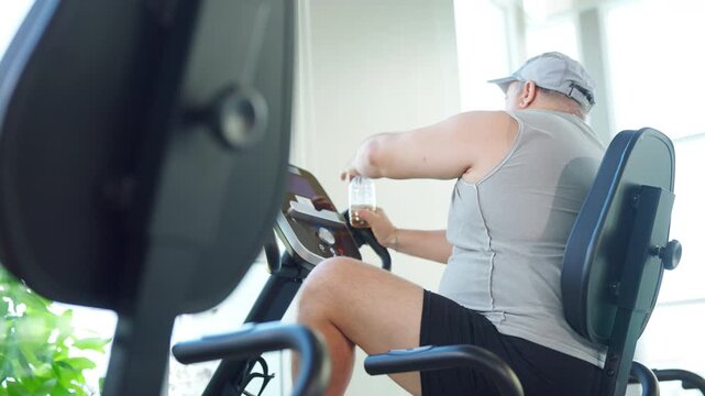Mature overweight man workout exercising on stationary exercise bike at fitness gym to improve health through cardio training for weight loss endurance active lifestyle healthy aging and wellness