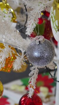 Christmas ornaments hanging on white artificial tree panning video footage silver glitter balls gold red decorations festive holiday season.