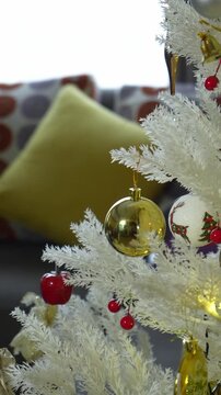 White christmas tree with gold ball and colorful ornaments vertical video footage cozy living room bokeh background festive holiday decoration. 