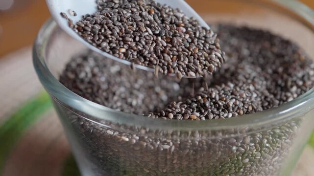 Spoon pouring chia seeds into glass jar closeup video footage healthy superfood and nutrition concept. 