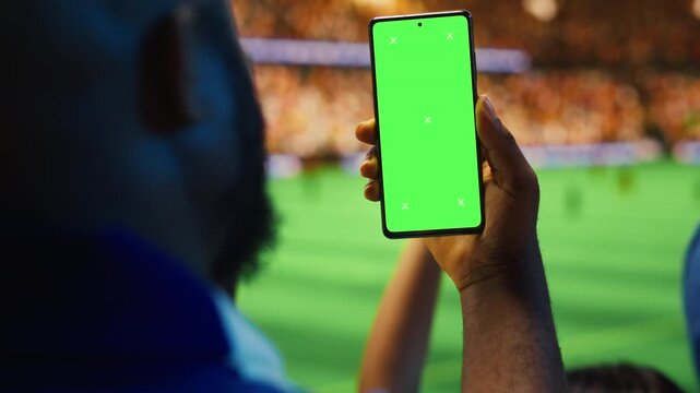 Chroma key smartphone used by football supporter celebrating winning match bet, pumping fists for sports betting, editable screen and fan reaction content.