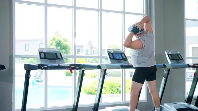 Mature overweight man stretching body after treadmill workout exercise at fitness gym improving flexibility muscle recovery healthy wellness lifestyle routine active aging and fitness sport training