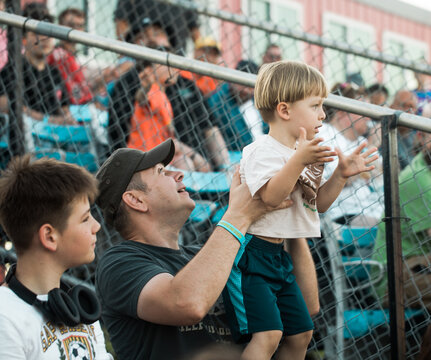A father and his two sons sitting in the stadium stands, cheering and supporting their favorite team. A happy family enjoying a sports event together, showing excitement, teamwork, and the spirit 
