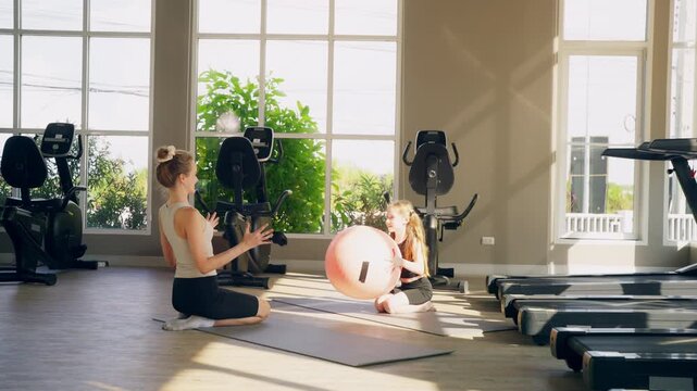 Mother teaching young daughter balance workout exercise on stability ball at fitness gym. Family fitness child development healthy active lifestyle healthcare living parent bonding and sport training